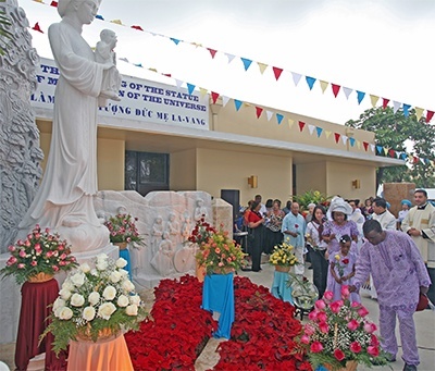 Nigerian-Americans Emanuel Okwor, Rita Okwor, 7, and her mother, Rita Okwor, place flowers at the foot of the new Marian shrine along with other St. Helen parishioners.
