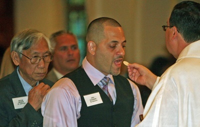 Jose Santiago, a candidate from St. Edward Church in Pembroke Pines, is accompanied by his sponsor, Trevor Chong, as he receives his first Communion from Father Carlos Vega, pastor of St. Bernard Church in Sunrise.