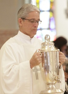 A deacon brings up the the oil of chrism which is used in confirmations and ordinations.