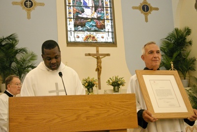 Father Chanel Jeanty, archdiocesan chancellor for canonical affairs, reads the Vatican document conferring the status of a minor basilica on St. Mary Star of the Sea in Key West, as a parishioner Tony Herce serving as an acolyte holds up the framed original.