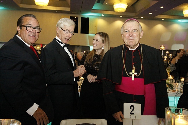 Archbishop Thomas Wenski and John Dooner, left, prepare to sit down to dinner as Katie Blanco-Crocquet, president of the archdiocesan Development Corporation, chats with Bob Dickinson.