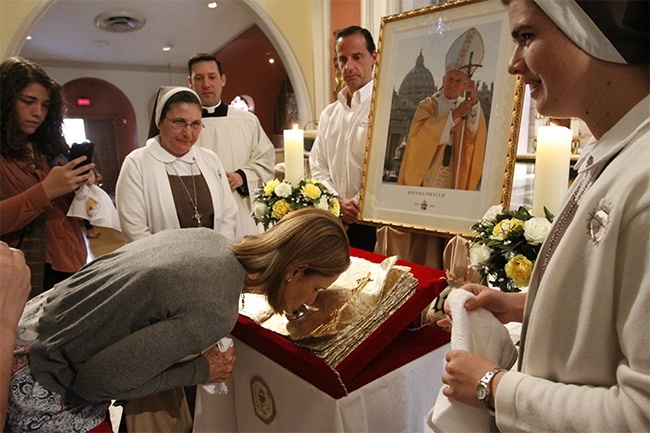 Siervas de los Corazones Traspasados de pie a los costados mientras la gente venera la reliquia del Papa Juan Pablo II.