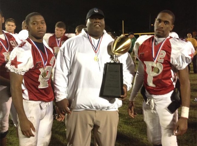 Carroll High seniors Leroy Clark (left) and D�Andre Smith (right) pose with Coach Raviel Maisonet, who is holding the victory trophy after the third annual Private vs. Public All Star High School Game.