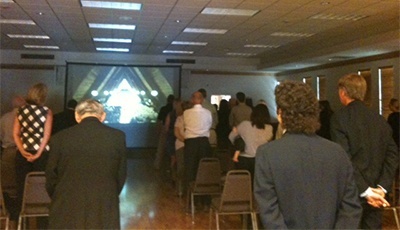 Crowd in the overflow room follows the Mass on a giant TV screen.