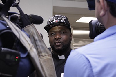 Wearing the Miami Heat championship cap, Msgr. Chanel Jeanty addresses local media.
