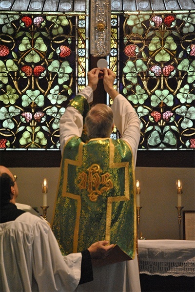Father Joseph Fishwick elevates the host during consecration. In the Extraordinary Form of the Mass, the priest faces ad orientem ("to the East") in the same direction as the rest of the congregation: toward God. The posture of the community is not oriented toward the priest, because Mass is considered a conversation with God, not the celebrant.