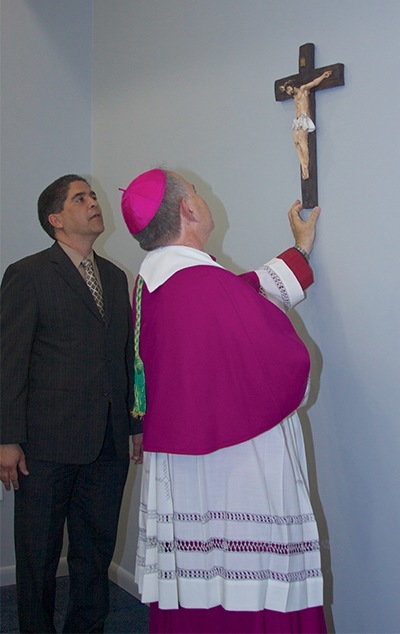 Bishop Fernando Isern, bishop emeritus of Pueblo, Colo.,  places a cross near the entrance of the Christopher Columbus High School's new All Sports Fitness Complex & Bernhardt Wellness Center.