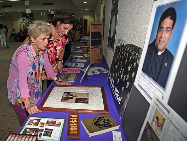 Aida Costales, a St. Louis parishioner since 1985, and Barbara Ludovici, parishioner since 1963, search through a seminary class photo looking for Father Michael Kish, now retired, a longtime St. Louis parochial vicar. A photo of current parochial vicar Father Biju Vells, also a former parishioner, is in the foreground.