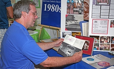 Chris Sailsbury, a St. Louis parishioner for 30 years, looks at a booklet showing the newly-constructed church in 1980.