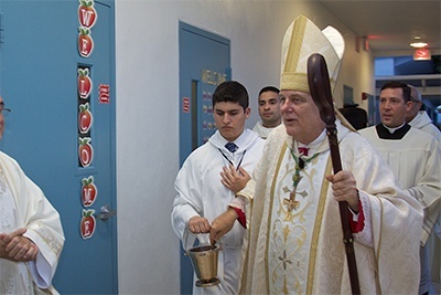 Archbishop Thomas Wenski sprinkles holy water on the exterior walls of the first floor of the Father Joseph T. Carney Enrichment Center.