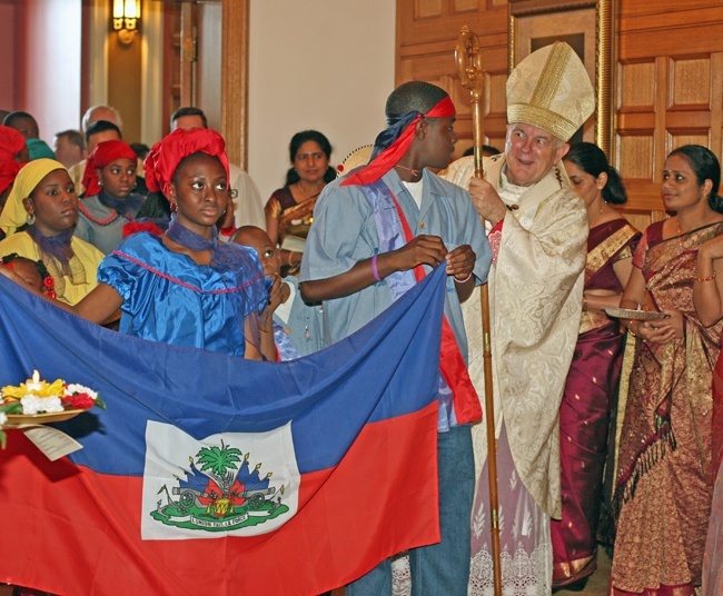 Archbishop Thomas Wenski chats with participants in the processsional for the Migration Mass, including Galvin Decius, 16, as Regine Destin, 13, holds the other end of the Haitian flag.