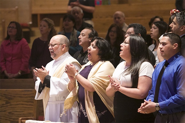 Deacon Pedro Toledo sings the Gloria during the Mass of ordination alongside his wife, Betsy, daughter Eilyn, and her husband, Victor Molina.