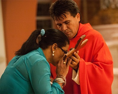 Ana LaRosa kisses the cross as Father Alvaro Pinzon holds it.