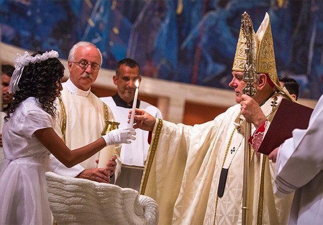 During the annual Easter Vigil Mass at St. Mary's Cathedral, Miami Archbishop Thomas Wenski hands a candle to catechumen Jasmin Rodas.