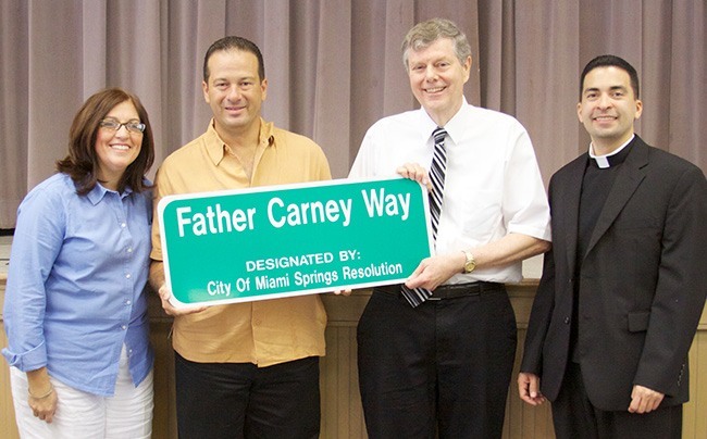 Miami Springs Mayor Zavier Garcia, center-left, and Tim Carney, brother to the late Father Joseph Carney, hold a replica of the street sign dedicated to the priest's memory. At left is Blessed Trinity School principal Maria Teresa Perez and at right is the parish administrator, Father Jose Alfaro.