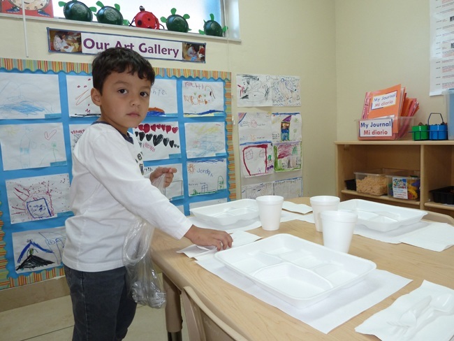 Justin Calix, 5 years old, sets the table for lunch time in his pre-k class.