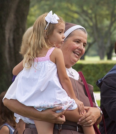 Sister Delia Morales, of the Servants of the Pierced Hearts, carries Blessed Trinity School student Carolina Coello during the eucharistic procession, giving the 5-year-old a short break from the mile and a half walk.