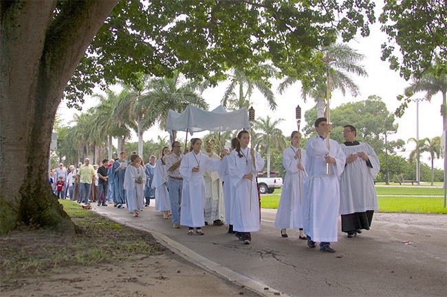 Father Jose Alfaro, Blessed Trinity's administrator, holds the monstrance and leads the eucharistic procession while members of the parish community hold the canopy and others process behind them.  The procession led parishioners from the church to the center of Miami Springs near the Circle. The entire route was nearly one and a half miles. The choir led the group in song and members of the Emmaus community led the group in the rosary.