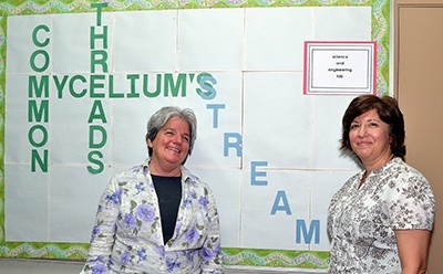 Carrie Roach, left, and Annette Buscemi show a poster at St. Helen School. Roach designed the poster after learning that threads of the Mycelium fungus can interlink to form a circle.