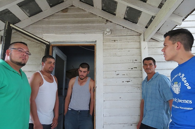 Miami seminarians Andres Pareja (left) and Nick Toledo (far right) spend time listening to Mexican migrant workers on the porch of the old farmhouse where they live.