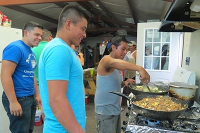 Miami seminarian Nick Toledo (left) watches migrant workers who have the evening’s cooking duty for their camp.