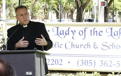 Father Jose Alvarez, current pastor of Our Lady of the Lakes Church, speaks at the ceremony renaming a street sign in front of the parish in honor of his predecessor, Father James Murphy.